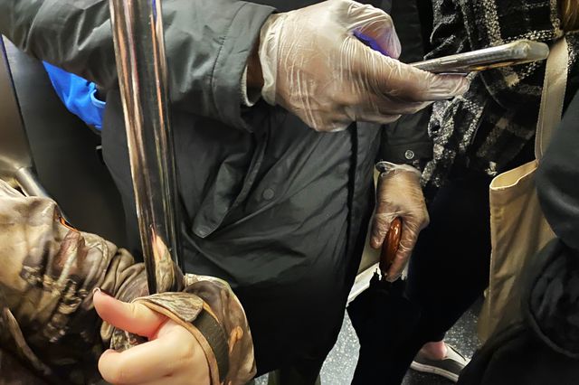 A man wears latex gloves on the subway while a woman uses her coat to hold the subway pole.